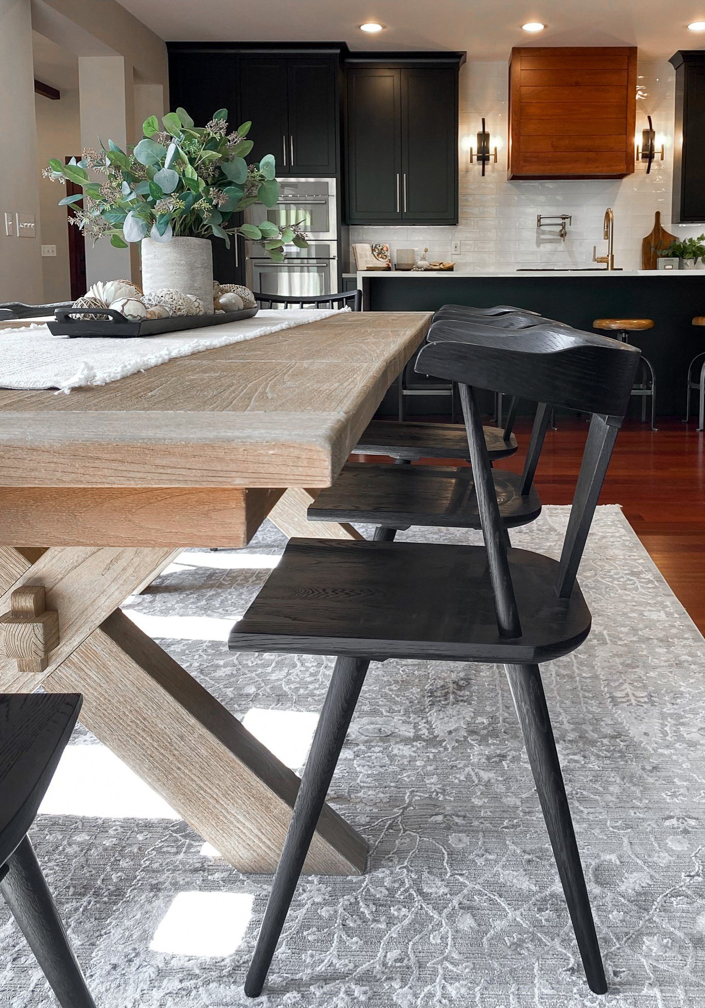 Dining room table with modern black wooden chairs, light toned table and grey area rug.