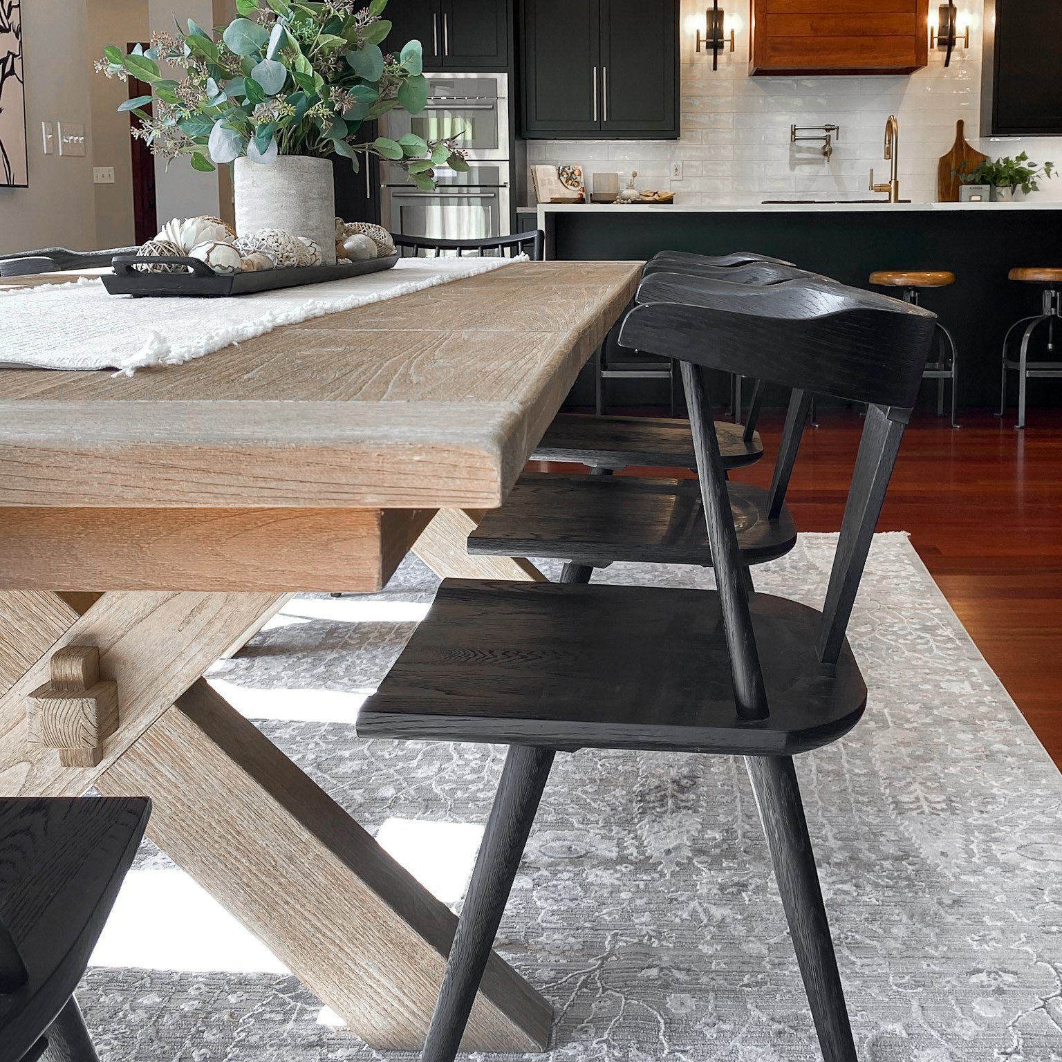 Dining room table with modern black wooden chairs, light toned table and grey area rug.